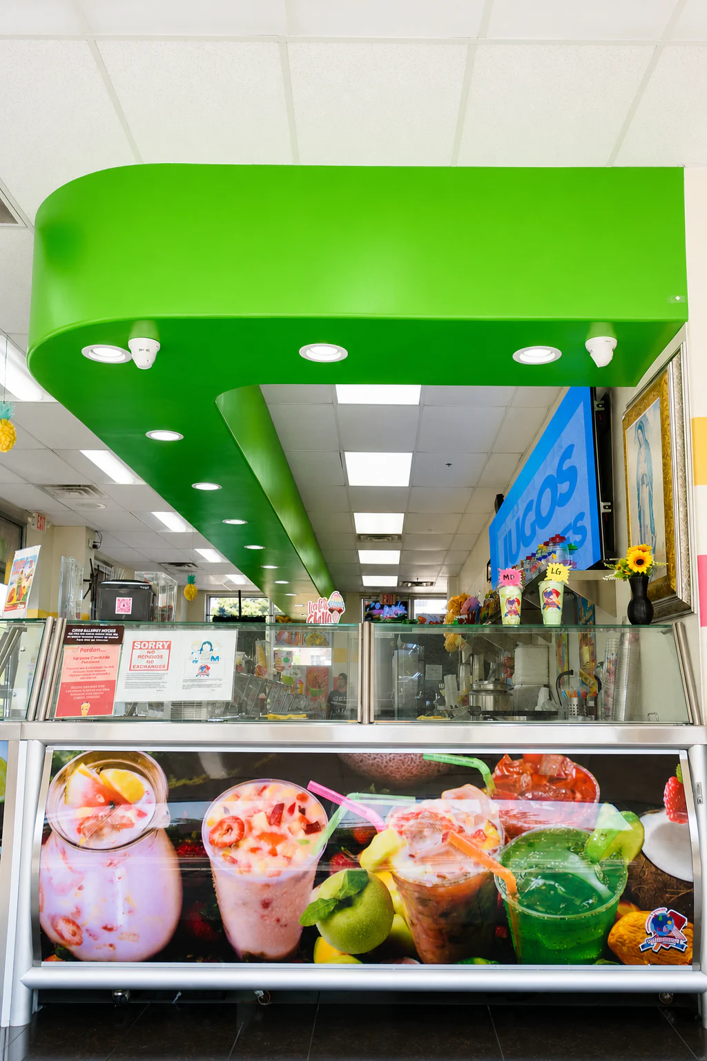 Inside La Michoacana Premium Oak Lawn: the bright green-canopied counter, a JUGOS sign, and a display case covered in colorful fresh-drink graphics.